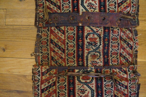 Red, navy, and beige flatweave textile with distressed leather trim rests on wood flooring.