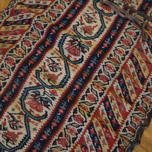 Flatwoven rug fragment featuring red, navy, and beige striped floral patterns on hardwood.