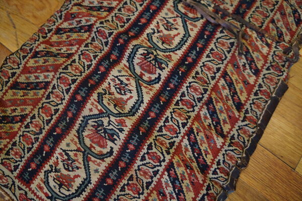 Flatwoven rug fragment featuring red, navy, and beige striped floral patterns on hardwood.