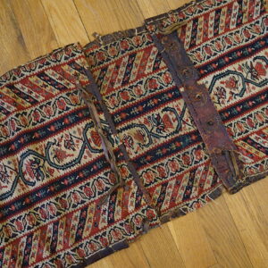 Segmented red, navy, and cream flatweave textile with stylized patterns and weathered leather straps on hardwood.