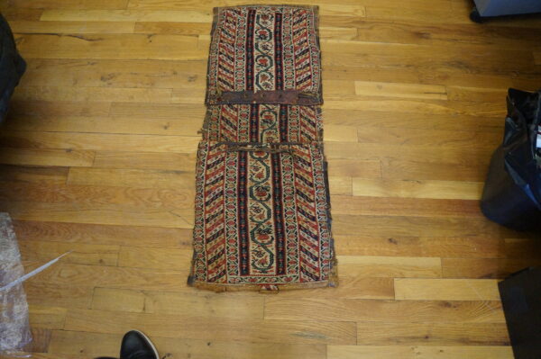 Red and navy patterned flatweave bag face or saddlebag with leather straps rests on a wood floor.