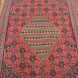 Red traditional runner rug featuring intricate patterns and a large central green and grey geometric medallion on a wood floor.