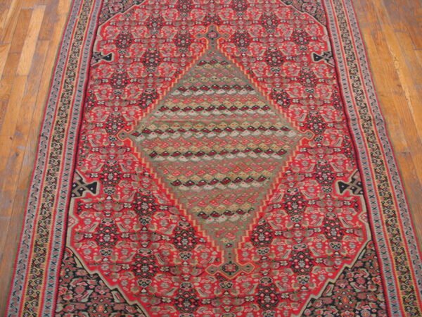 Red traditional runner rug featuring intricate patterns and a large central green and grey geometric medallion on a wood floor.