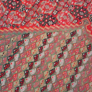 Low-pile rug detail showing red floral patterns transitioning to a green field with repeating geometric shapes.