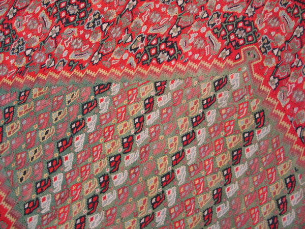 Low-pile rug detail showing red floral patterns transitioning to a green field with repeating geometric shapes.