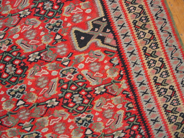 Coarse, red medium-pile rug detail featuring colorful dense patterns and layered geometric borders on wood flooring.
