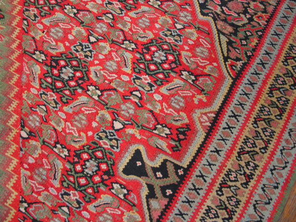 Intricate flatwoven rug featuring a bright red field with floral and geometric motifs and multi-colored striped borders.