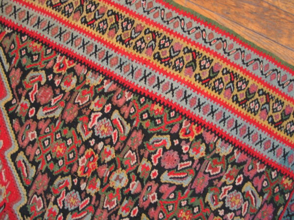 Detail of a vibrant rug with floral motifs, black ground, and multiple red, blue, and gold borders on wood.