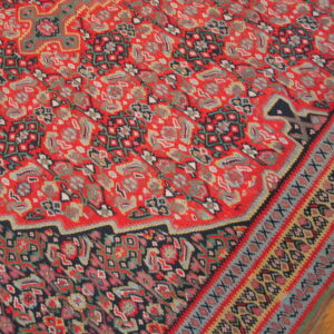 Red rug with dense, multicolored floral and geometric patterns resting on light wood flooring.