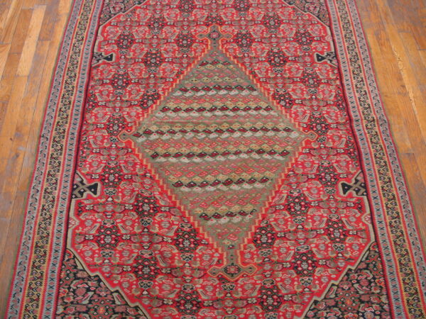 Ornate runner rug featuring a red field, geometric border, and a large green diamond center on wood flooring.