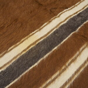 Long-pile shaggy rug displaying wide diagonal stripes of brown, cream, and charcoal on wood plank flooring.