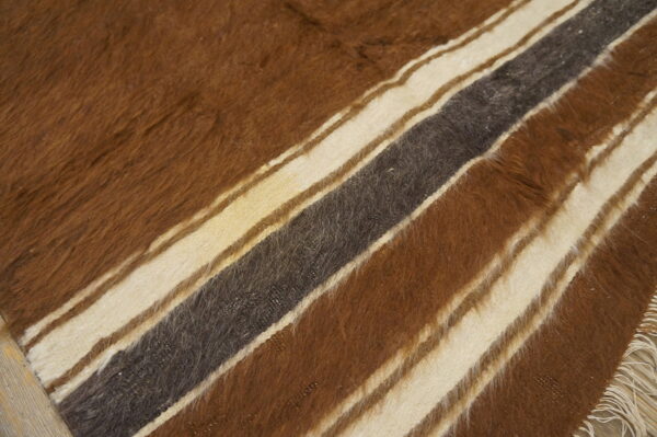 Long-pile shaggy rug displaying wide diagonal stripes of brown, cream, and charcoal on wood plank flooring.