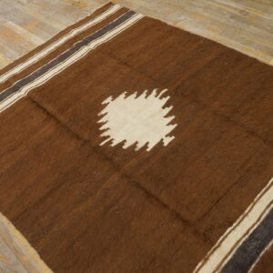 Brown high-pile rug with a cream sawtooth center medallion and striped edges over light wooden planks.