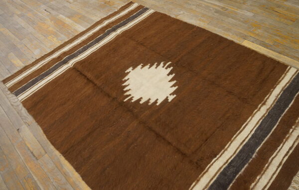 Brown high-pile rug with a cream sawtooth center medallion and striped edges over light wooden planks.