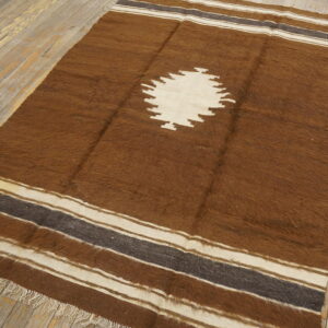 A shaggy brown rug featuring a large cream diamond motif and striped borders rests on distressed wood floorboards.