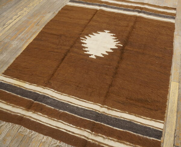 A shaggy brown rug featuring a large cream diamond motif and striped borders rests on distressed wood floorboards.