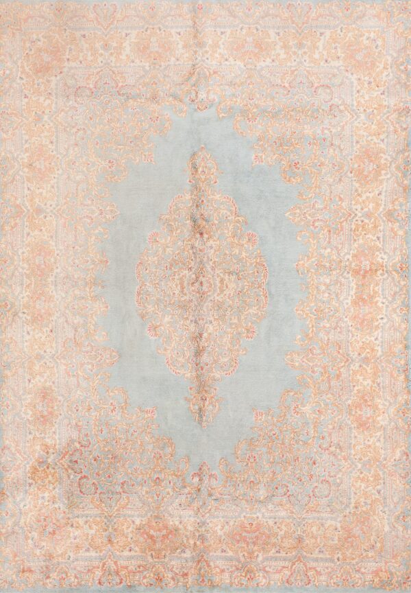 Ornate medallion rug featuring dusty blue, tan, and faded pink designs rests on dark wood planks.