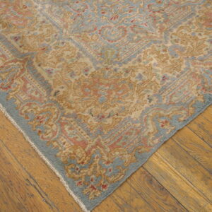 Ornate tan, blue, and coral patterned rug corner resting on rustic golden wood plank flooring.