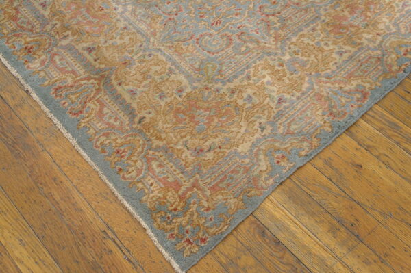 Ornate tan, blue, and coral patterned rug corner resting on rustic golden wood plank flooring.