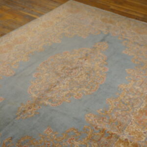 Faded blue rug with traditional gold and rose motifs displayed on polished wooden planks.