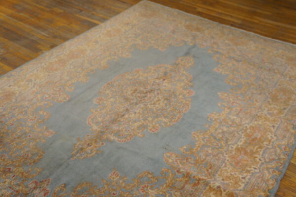 Faded blue rug with traditional gold and rose motifs displayed on polished wooden planks.