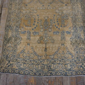 Distressed camel rug with faded indigo borders and pattern lays on rustic grey wood flooring.