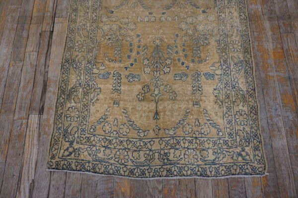 Distressed camel rug with faded indigo borders and pattern lays on rustic grey wood flooring.
