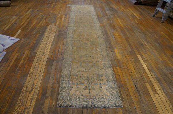 Faded gold runner rug with blue traditional patterns resting on old plank wood floors.