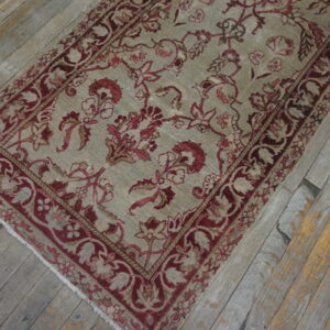 Muted beige rug with a dense burgundy floral design rests on worn gray and yellow wood planks.