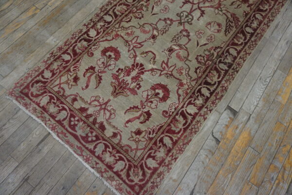 Muted beige rug with a dense burgundy floral design rests on worn gray and yellow wood planks.
