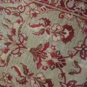 Detailed low-pile rug with red floral medallions and borders on a muted grayish-green field.
