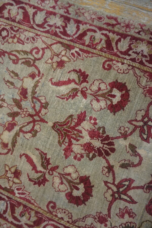 Detailed low-pile rug with red floral medallions and borders on a muted grayish-green field.