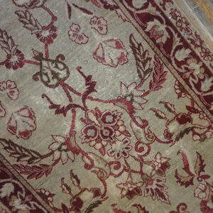 Faded rug showing burgundy and beige botanical patterns on a muted pale green field over wood planks.