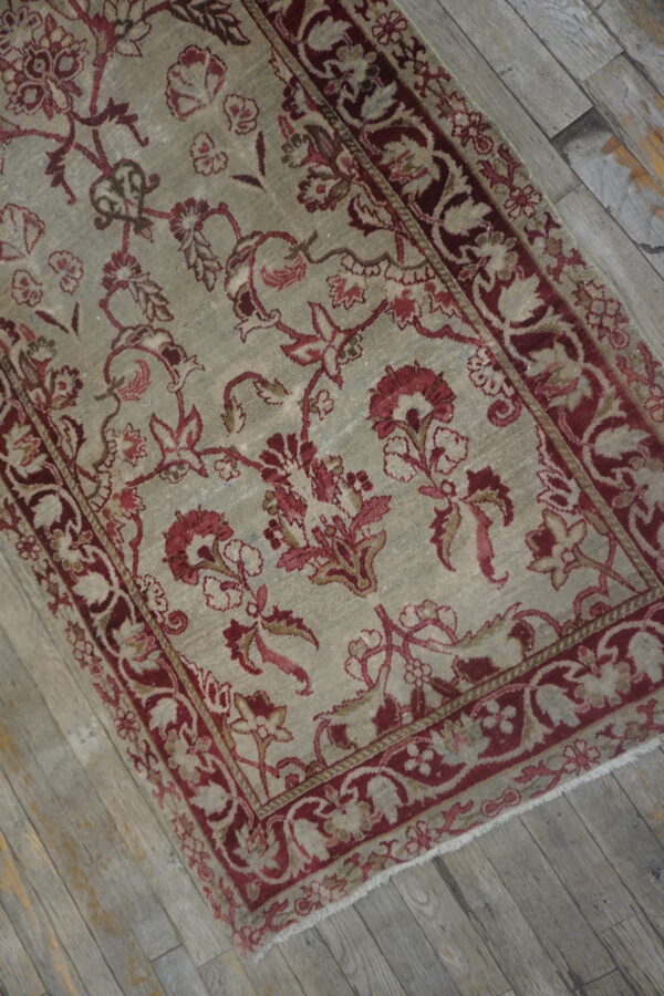 A distressed sage and burgundy floral rug runner lies diagonally on rustic gray plank flooring.