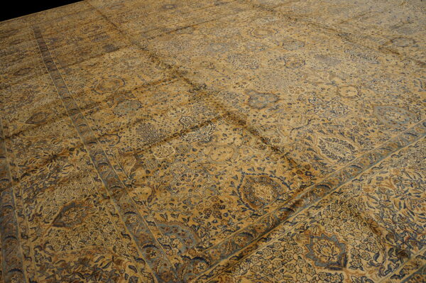 Detailed view of a gold and blue traditional rug with intricate floral patterns and wide borders.