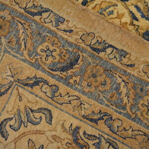 Detail close-up of a low-pile gold and navy traditional rug showing intricate borders and a fold.