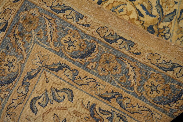 Detail close-up of a low-pile gold and navy traditional rug showing intricate borders and a fold.