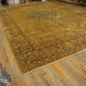An oversized ochre rug with complex navy and brown floral designs rests on worn light wood planks.