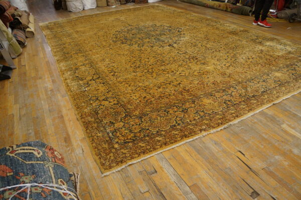 An oversized ochre rug with complex navy and brown floral designs rests on worn light wood planks.