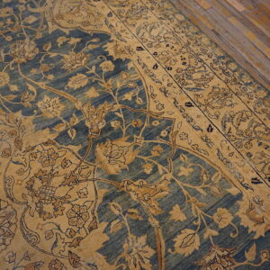 Gold floral patterns cover a distressed blue rug placed on worn wooden flooring.