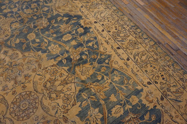 Gold floral patterns cover a distressed blue rug placed on worn wooden flooring.