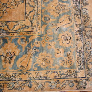 Corner detail of a traditional patterned rug in beige, muted blue, and dark blue on wood flooring.