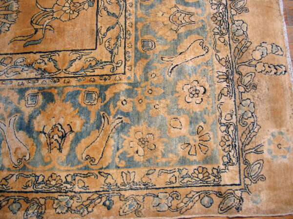 Corner detail of a traditional patterned rug in beige, muted blue, and dark blue on wood flooring.
