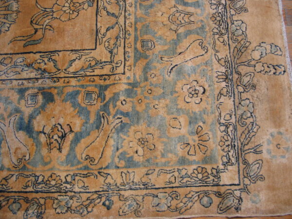 Close-up of an ornate rug featuring detailed tan and blue floral patterns and multiple borders on a wood floor.