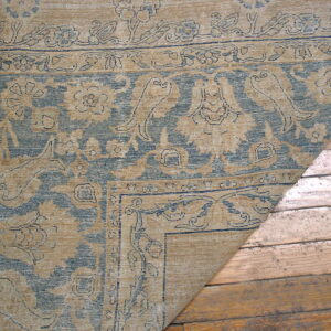 Traditional tan and blue patterned rug corner rests on rustic wooden floorboards.