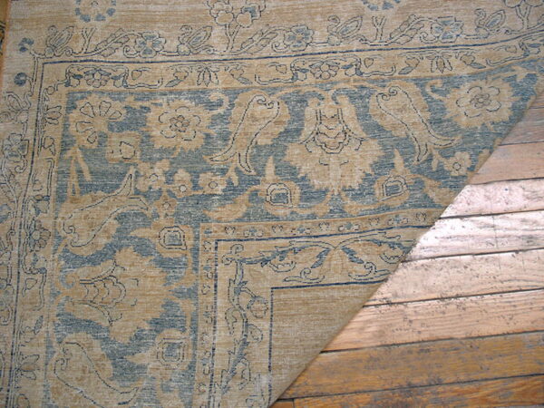 Traditional tan and blue patterned rug corner rests on rustic wooden floorboards.