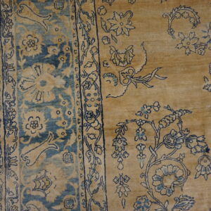 Ornate tan rug detail showing blue floral motifs, a border, and distressed gray plank flooring.