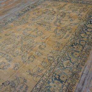 Gold and blue traditional low-pile rug featuring ornate florals lies on rustic wooden planks.