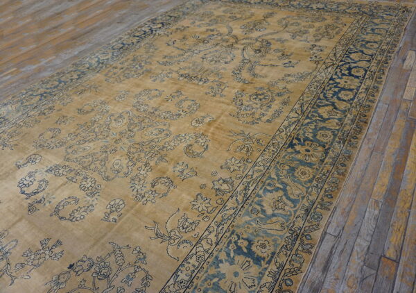 Gold and blue traditional low-pile rug featuring ornate florals lies on rustic wooden planks.