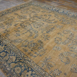 A large, distressed gold rug with elaborate blue and indigo floral patterns rests on weathered wood floors.